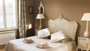 A neatly made bed with pillows and folded towels, a bedside table with a lamp, and a window with curtains. - Two bedroom apartment in the heart of Vaison la Romaine (Vaison-la-Romaine)