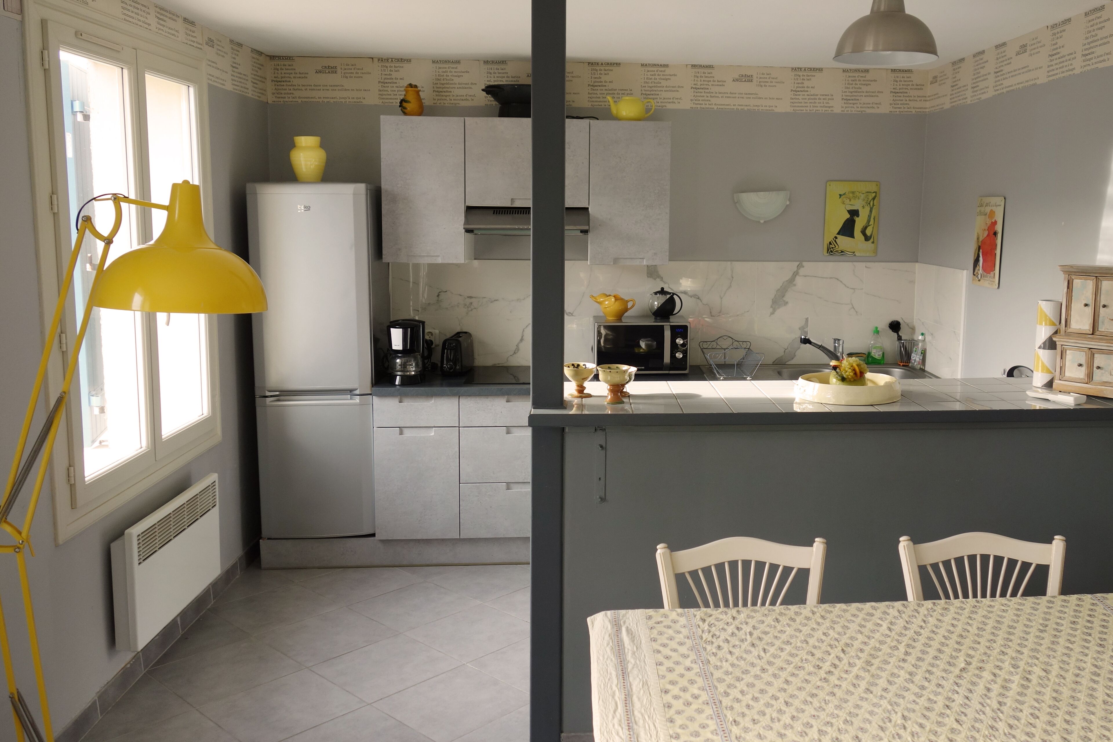 A compact kitchen with a refrigerator, coffee maker, microwave, and a small dining area with a table and chairs.
