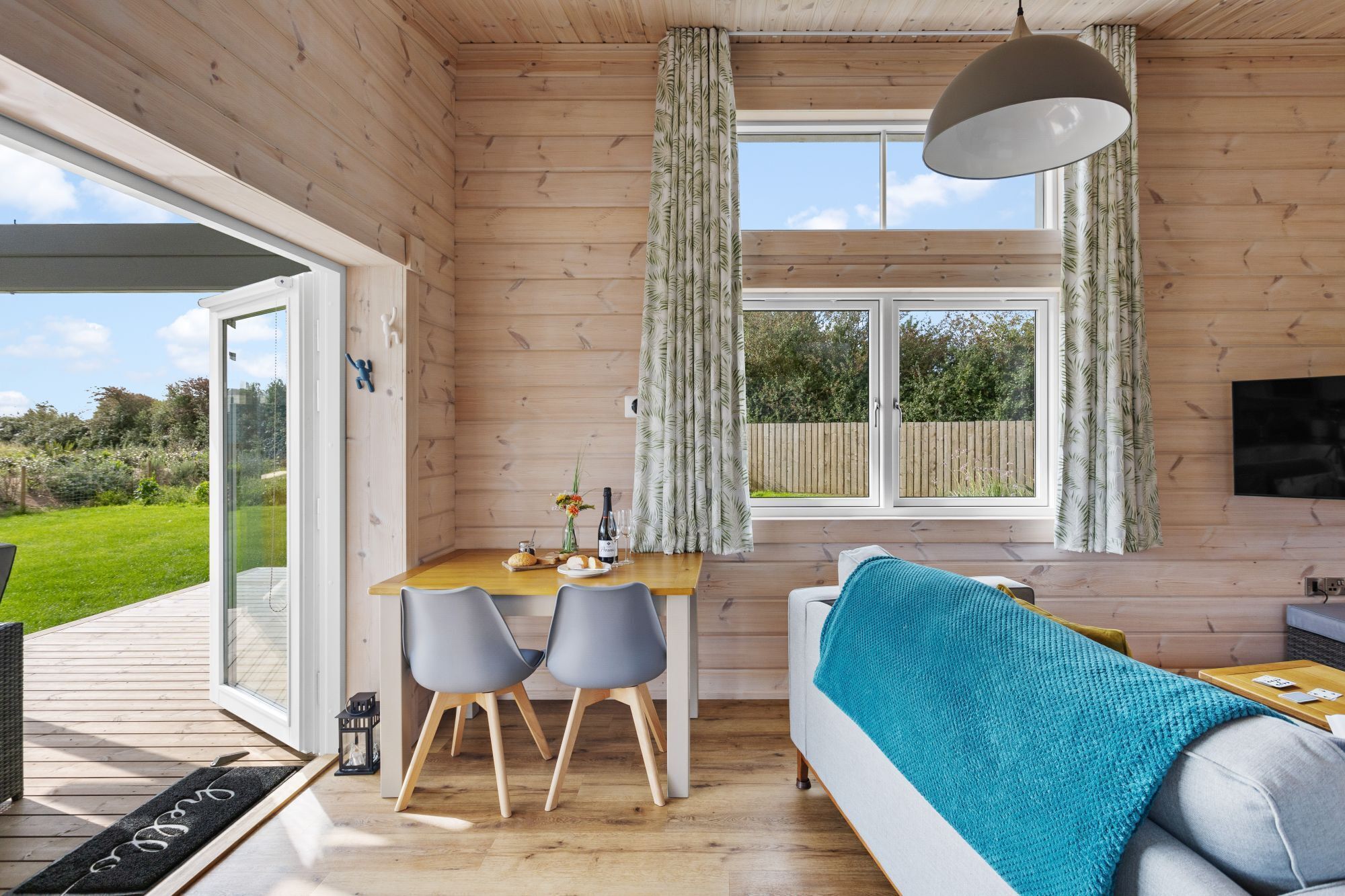 A wooden interior with a dining area, a sofa, and a large window.