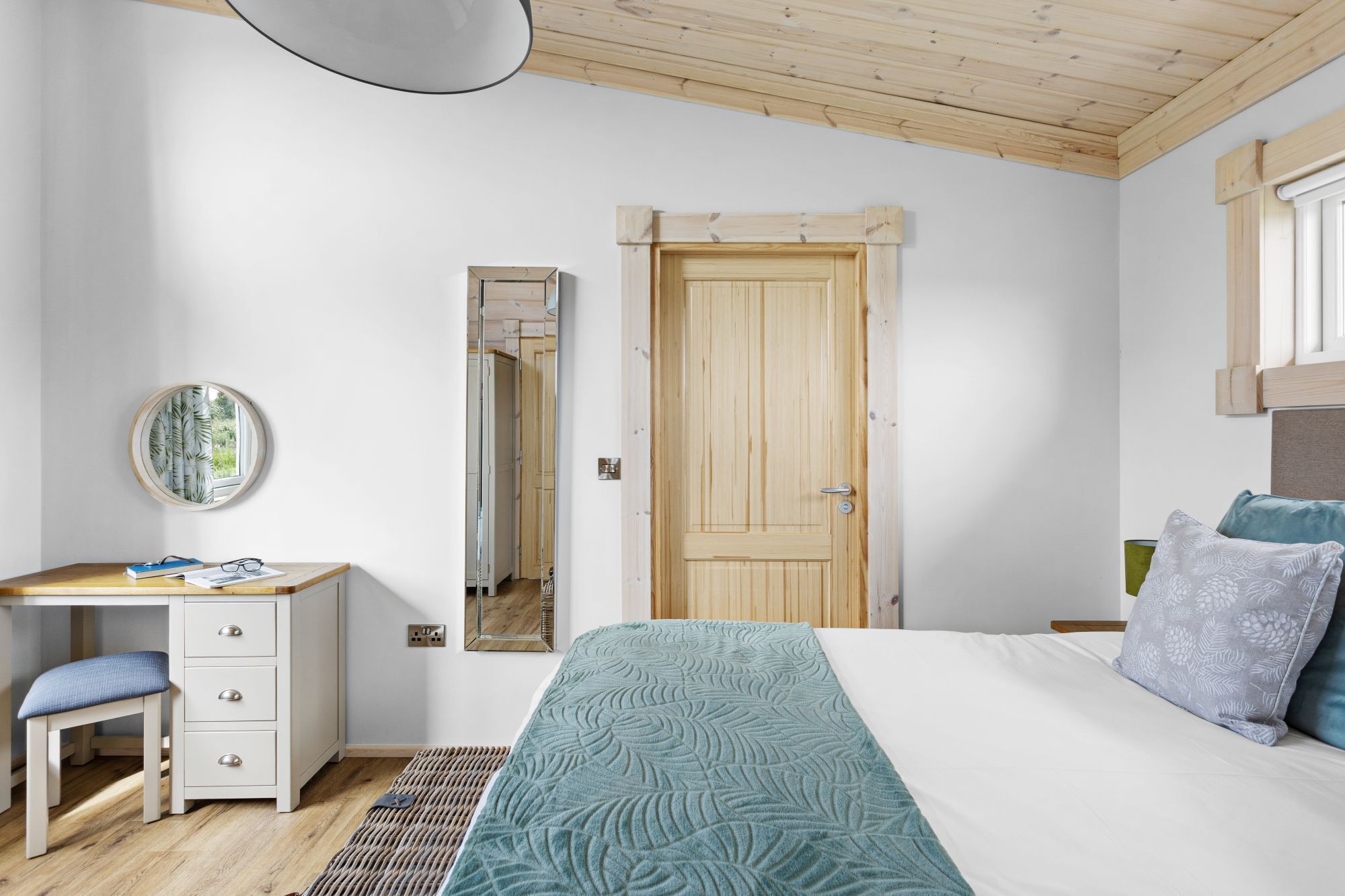 A bedroom with a bed, a desk with drawers, a mirror, and a window with curtains.