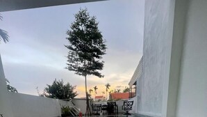 A swimming pool with tiled flooring, a table and chairs, and a tree in the background. - Moon house villa (Da Nang)