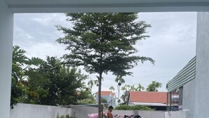An outdoor swimming pool with a clear view of the surrounding area, including a table and chairs, a tree, and a building in the background. - Moon house villa (Da Nang)