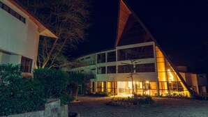 Un edificio moderno con techo inclinado y ventanas grandes, rodeado de vegetación.