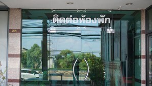 A hotel entrance with a glass door, a sign with Thai script, and a potted plant to the right. - The Popular place (Bang Phli)
