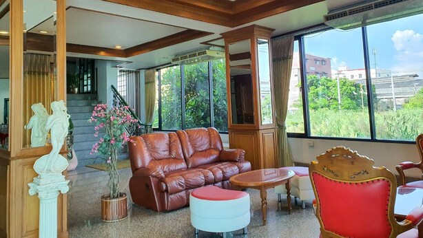 A spacious living area with a leather sofa, a small round table, and a red chair. There is a large window offering a view of greenery and buildings outside. - The Popular place (Bang Phli)