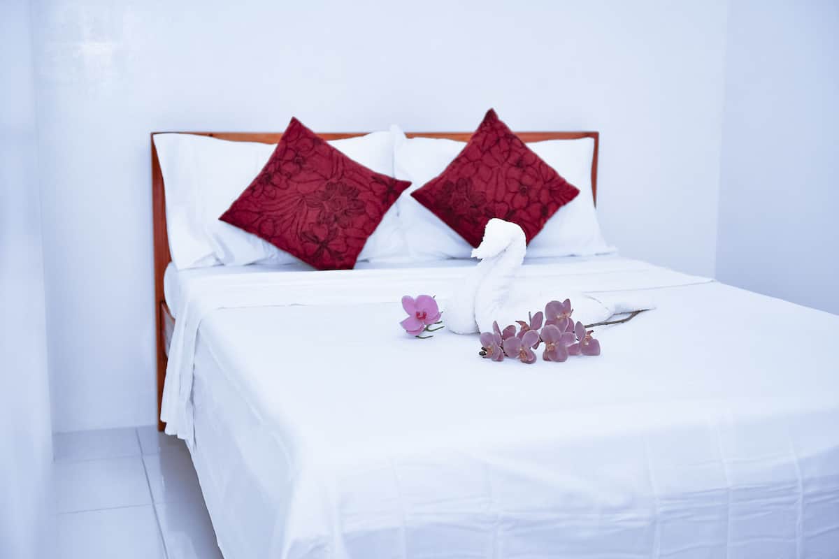 Un lit bien fait, avec une literie blanche et deux oreillers rouges, une tête de lit en bois et une décoration en forme de cygne posée sur le lit.