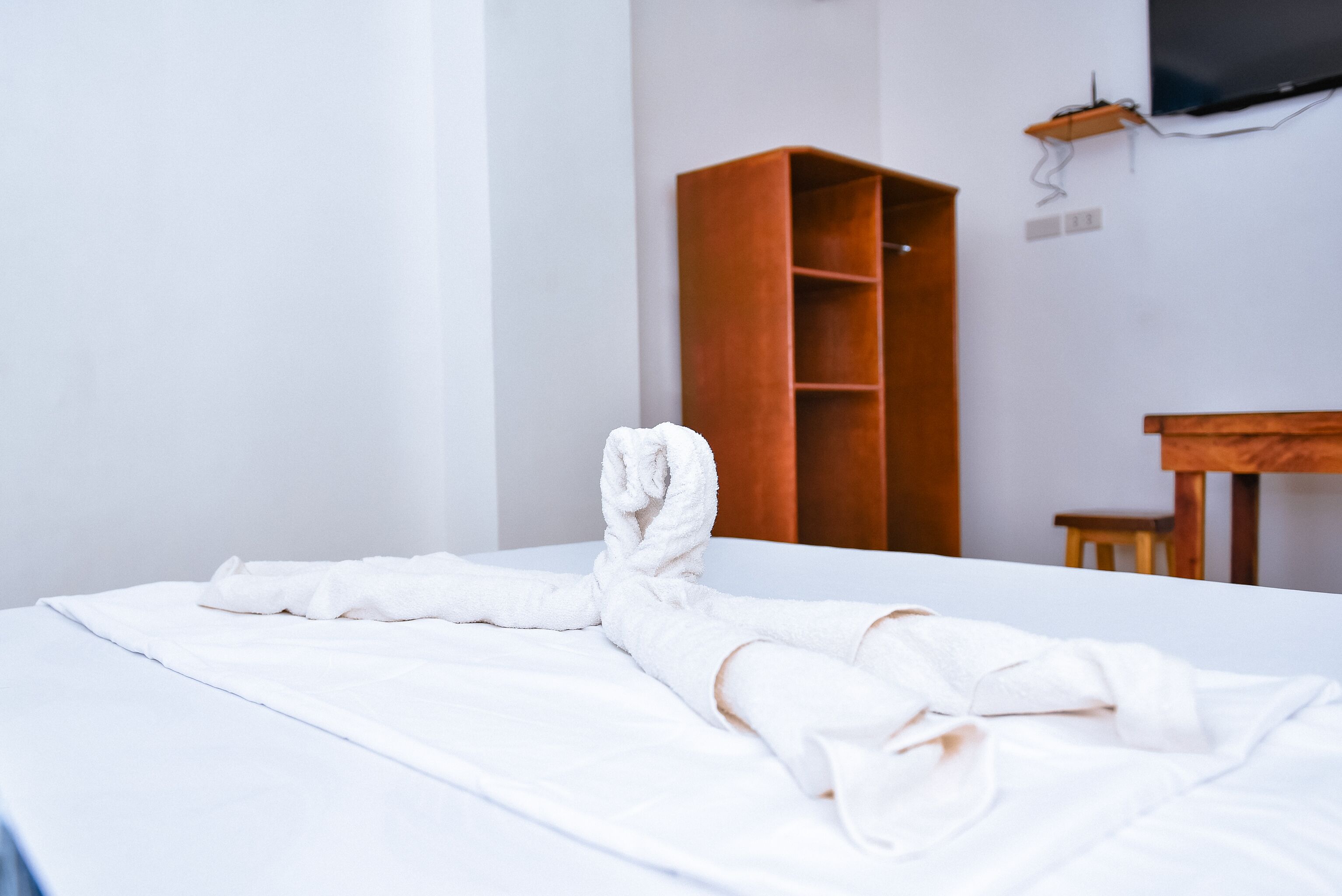 Ein Hotelzimmer mit einem ordentlich bezogenen Bett, einem Holzschrank und einem kleinen Holztisch.
