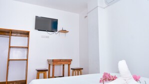 A hotel room with a bed, a wooden desk, a television mounted on the wall, and a wardrobe.