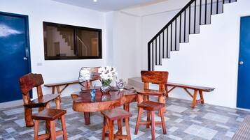 Uma área de refeições com mesa e cadeiras de madeira, um vaso com flores e uma escada com guarda-corpos pretos.