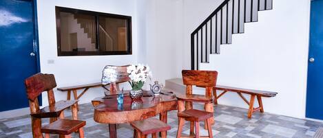 A dining area with a wooden table and chairs, a vase with flowers, and a staircase with black railings.