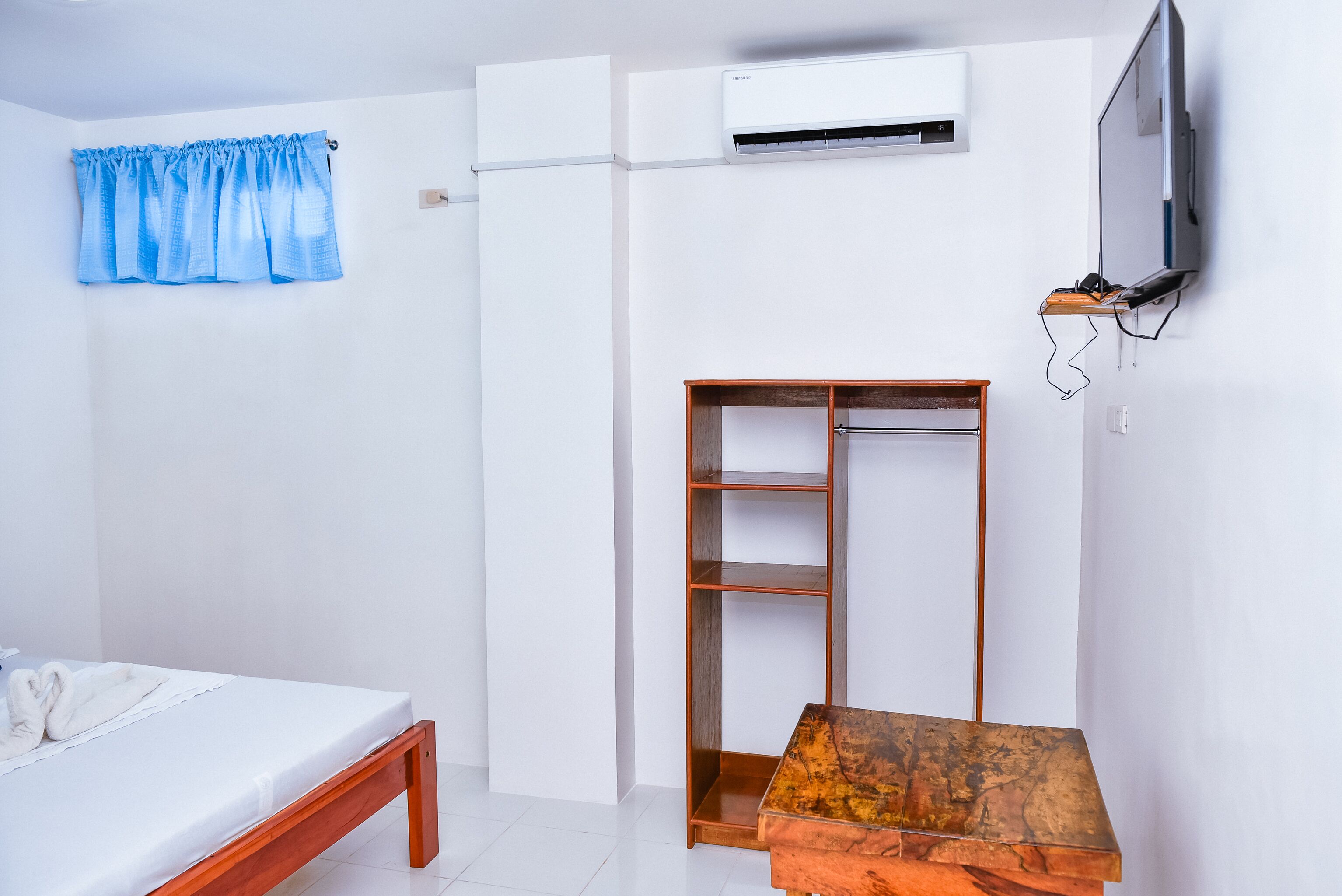 A bedroom with a bed, a wooden table, a wardrobe, and a television mounted on the wall.