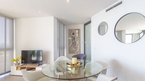 A modern living room with a glass dining table, white chairs, a flat-screen TV, and a large mirror on the wall. - Apartamento Bernia al Mar by Costa CarpeDiem (Calpe)