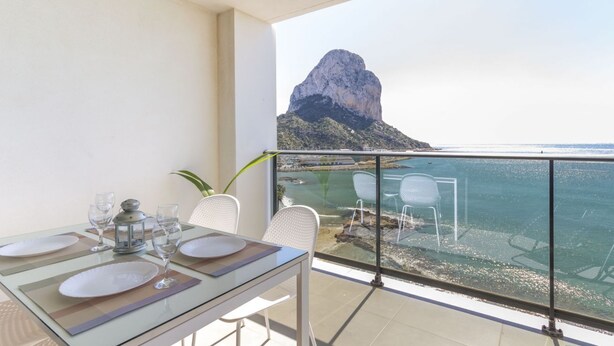 A balcony with a dining table set for four, overlooking a coastal view with a prominent rock formation. - Apartamento Bernia al Mar by Costa CarpeDiem (Calpe)