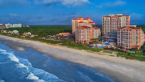 A beachfront hotel with multiple high-rise buildings, a sandy beach, and a pool area.