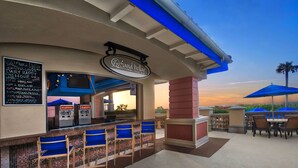 An outdoor bar area with a pool bar sign, seating, and a view of the sunset.