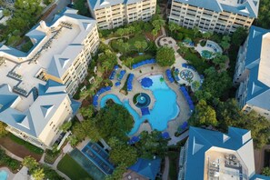 An aerial view of a hotel complex with multiple buildings, a central swimming pool, and surrounding greenery.