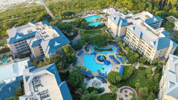 An aerial view of a resort with multiple buildings, a central swimming pool, and surrounding greenery.