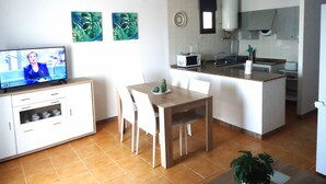 Un espai vital reduït amb zona de menjador, cuina i un televisor que mostra una persona.