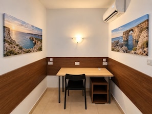 Une petite pièce avec une table et des chaises en bois, un luminaire fixé au mur et deux tableaux encadrés représentant des paysages côtiers.