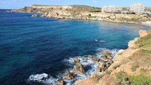 Un hotel frente al mar con varias edificaciones, costa rocosa y mar azul cristalino.