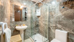 Un baño moderno con ducha envuelta en vidrio, lavabo pedestal y retrete.