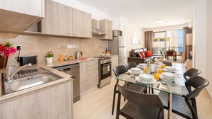 Una cocina moderna con zona de comedor, electrodomésticos de acero inoxidable y una mesa de vidrio lista para comer.
