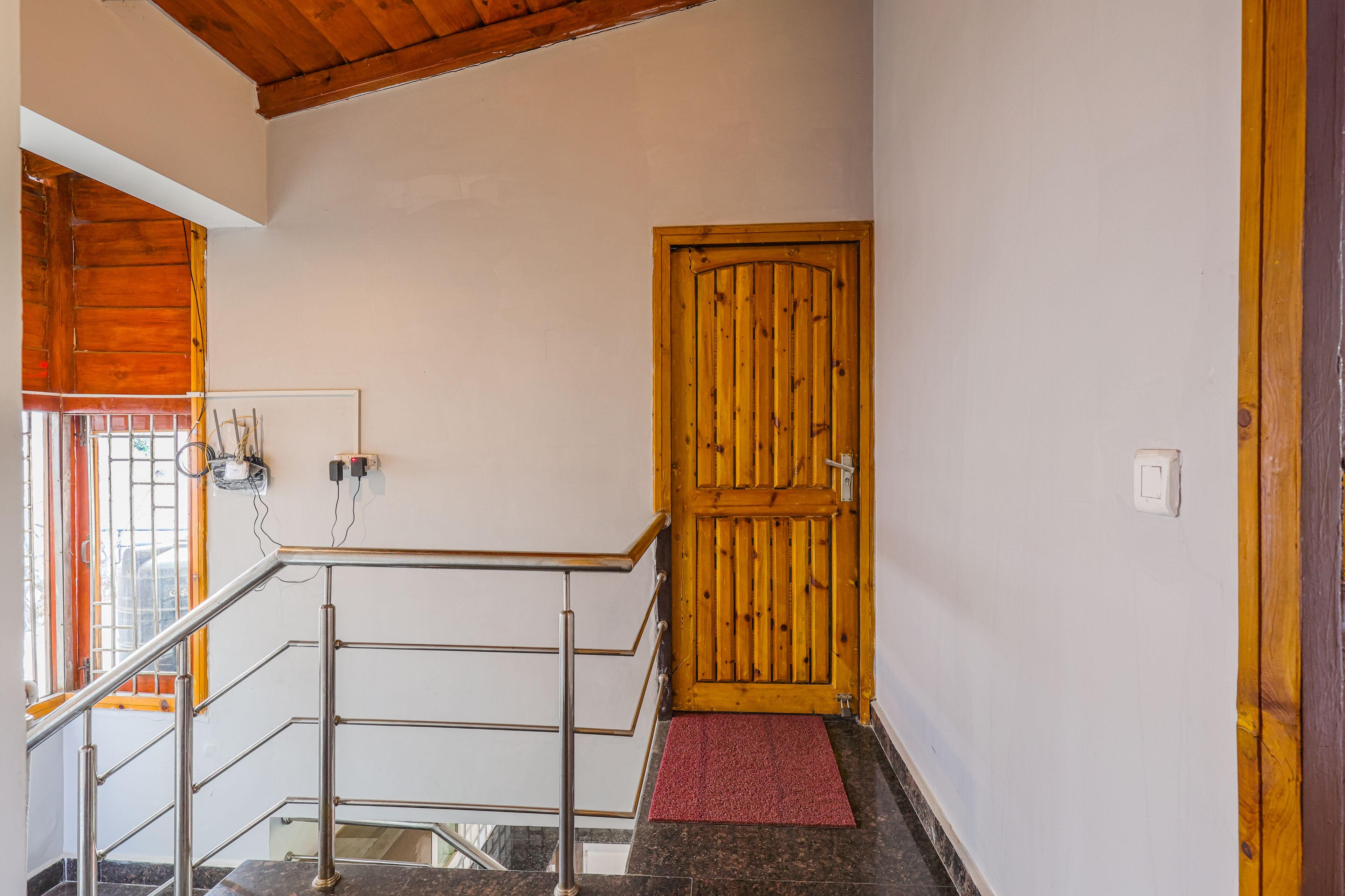 Un escalier avec une rampe métallique, une porte en bois et un tapis rouge au bas.