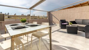 A rooftop terrace with a dining table set for four, surrounded by chairs, and a sofa area with cushions. - Michelangelo by Interhome (Salou)