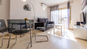 A modern living room with a glass dining table, black chairs, a grey sofa, a white coffee table, and a TV on a white cabinet. - Michelangelo by Interhome (Salou)