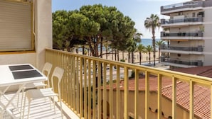 A balcony with a table and chairs, overlooking a beach with palm trees and a building with balconies. - Miramar Nautic by Interhome (Salou)