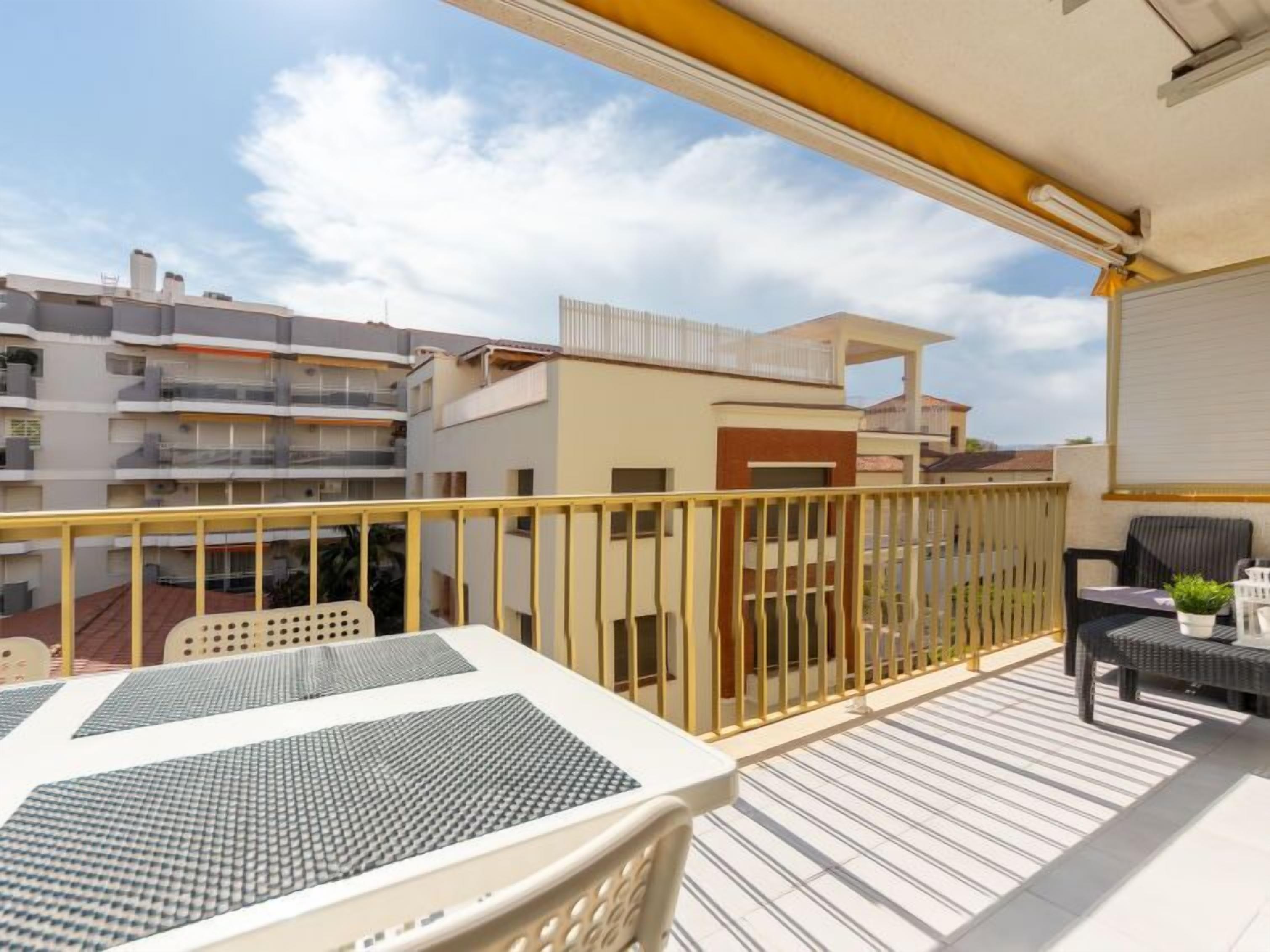 A balcony with a yellow railing, outdoor seating, and a view of neighboring buildings.