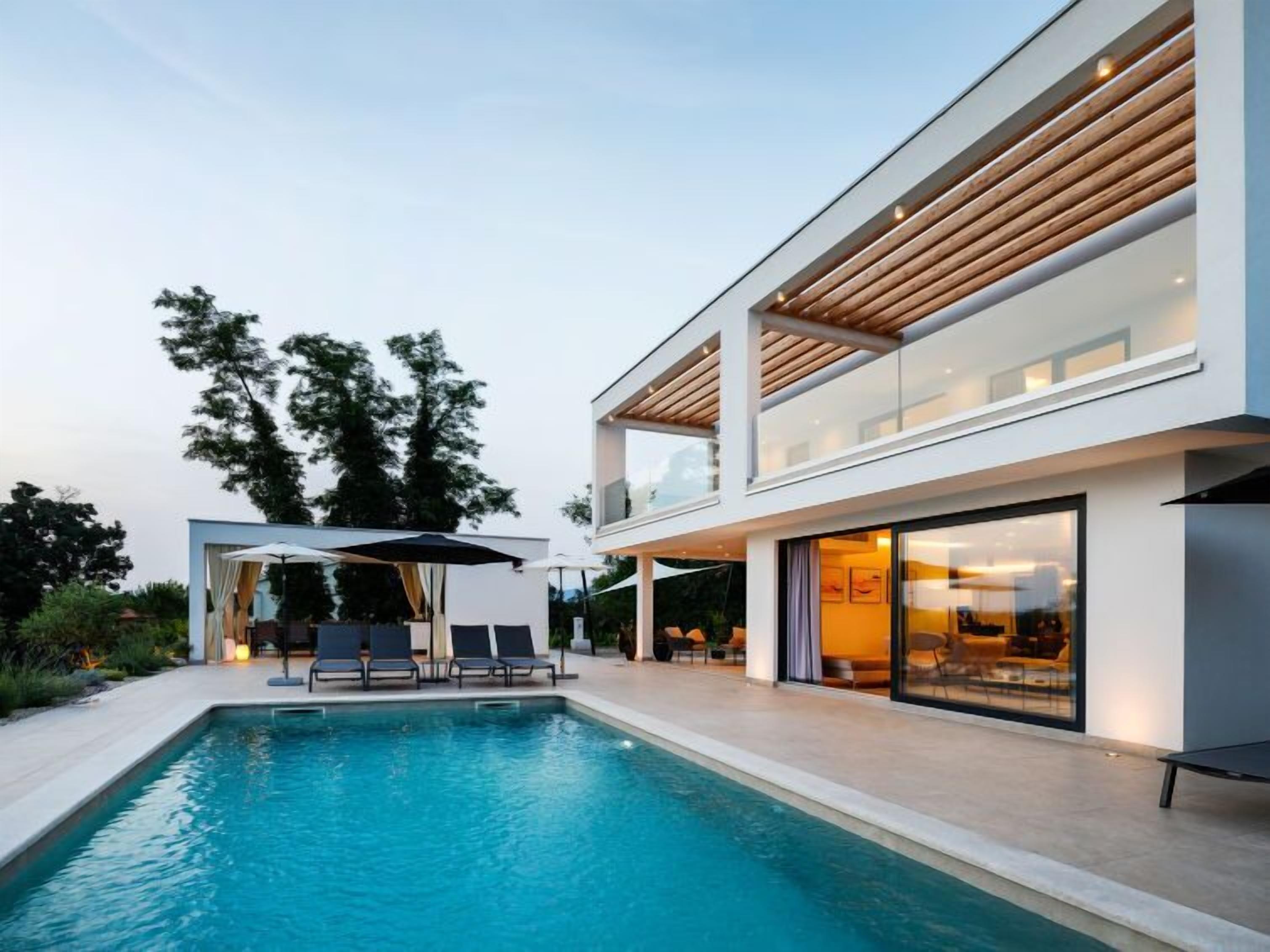 A modern two-story house with a swimming pool, outdoor seating, and large windows.