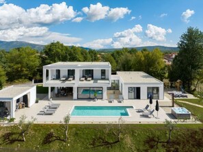 A modern two-story house with a swimming pool, outdoor seating, and a view of the surrounding landscape.