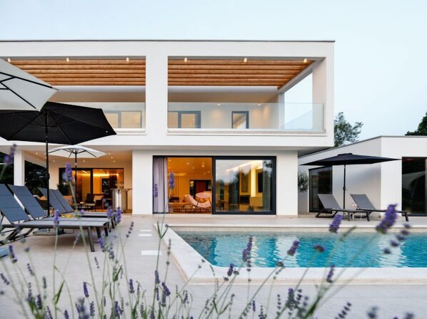 A modern two-story house with a swimming pool, outdoor seating, and a well-lit interior.