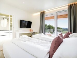 A modern hotel room with a large bed, a desk with a flat-screen TV, and a view of the outdoors.