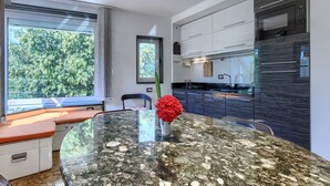 Una cocina moderna con horno empotrado, un ventanal grande y una zona de comedor con mesa de vidrio.