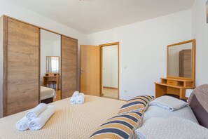 A hotel room with a bed, a wooden wardrobe, a desk with a chair, and a mirror.