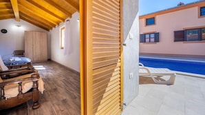 Camera da letto con soffitto in legno, un letto, un armadio e vista su una piscina.