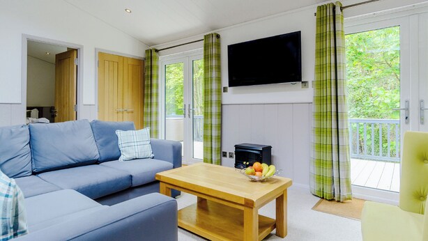 A living room with a sofa, a coffee table, a flat-screen TV, and a balcony with green curtains.