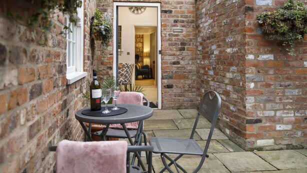 A brick exterior wall with a small patio area featuring a round table, two chairs, and a bottle of wine. - The Bingham, Fossgate  Apartments Central York (York)
