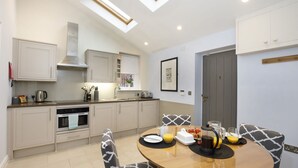 A modern kitchen with a dining area, featuring a round table, chairs, and breakfast items. - The Bingham, Fossgate  Apartments Central York (York)