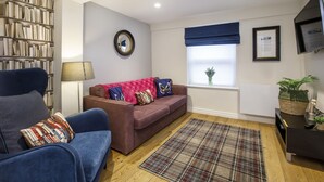 A living room with a blue sofa, a brown sofa, a plaid rug, a bookshelf, a mirror, a window with a blue valance, and a TV on a stand. - The Bingham, Fossgate  Apartments Central York (York)