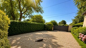 A gravel driveway leading to a gated entrance, surrounded by well-maintained hedges and trees.