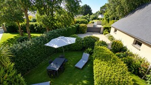 A well-maintained garden with a table and chairs, a sun umbrella, and a lawn.