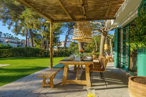 An outdoor patio with a wooden table set for dining, surrounded by wicker chairs and a hanging basket.