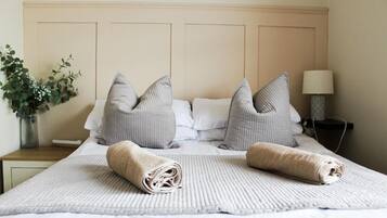 A neatly made bed with rolled towels, a bedside lamp, and a vase with greenery.