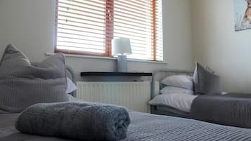 Une chambre à coucher avec un lit, une table de chevet avec une lampe, un radiateur et une fenêtre avec des stores.