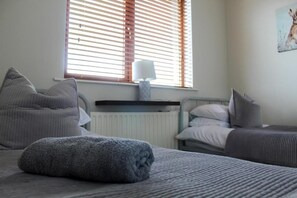 Ein Schlafzimmer mit einem Bett, einem Nachttisch mit Lampe, einem Heizkörper und einem Fenster mit Jalousien.