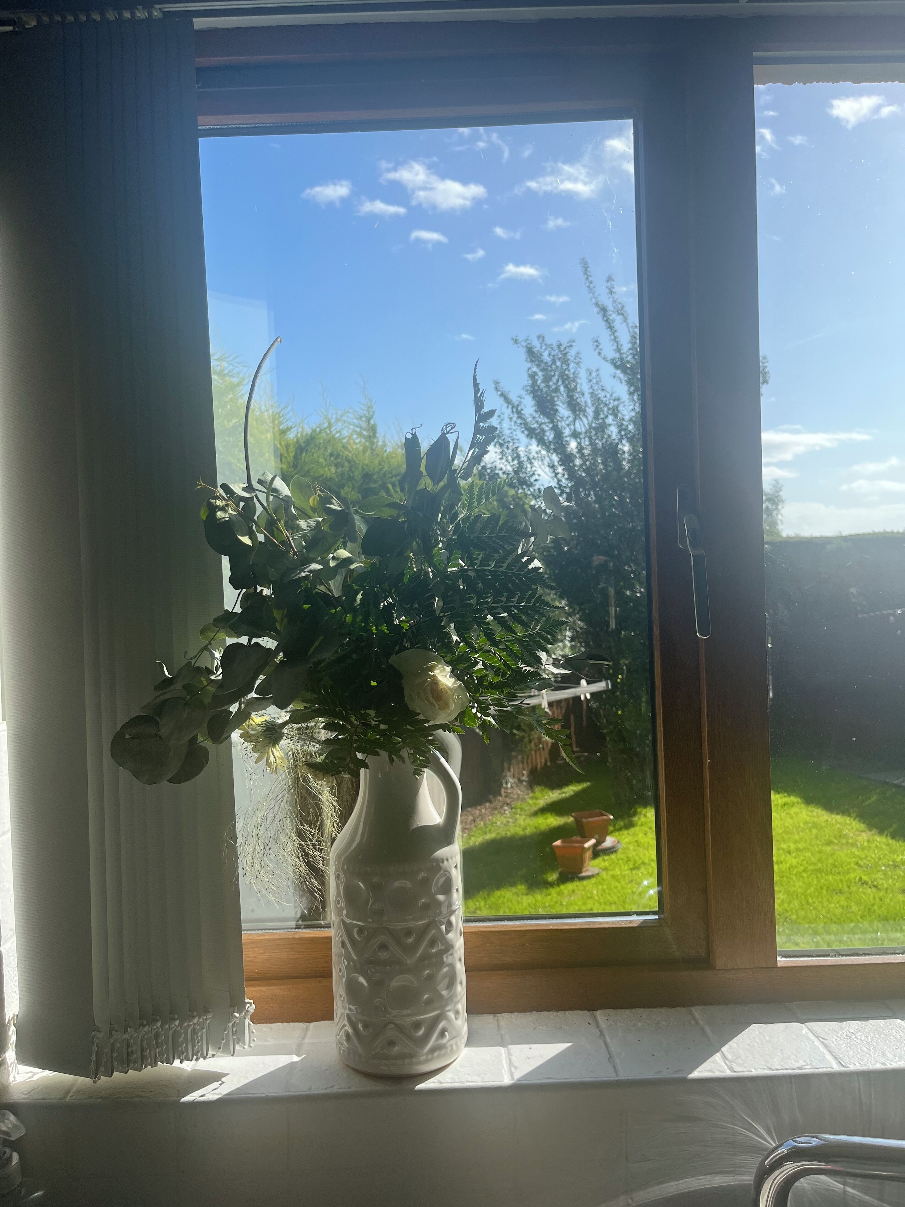 Un jarrón blanco con una planta en un alféizar.