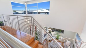A modern interior with a wooden staircase, metal railings, and large windows offering a view of buildings and greenery.